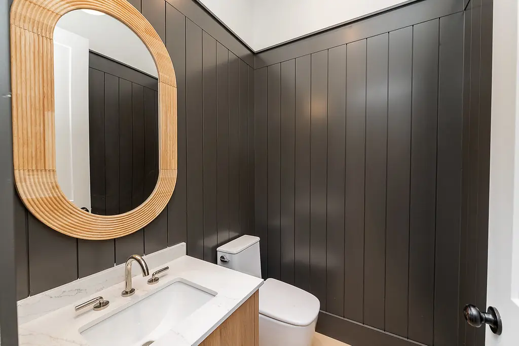 Powder room with dark panelled wall and oval oak mirror